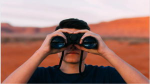 Image of a man in a desert looking through binoculars